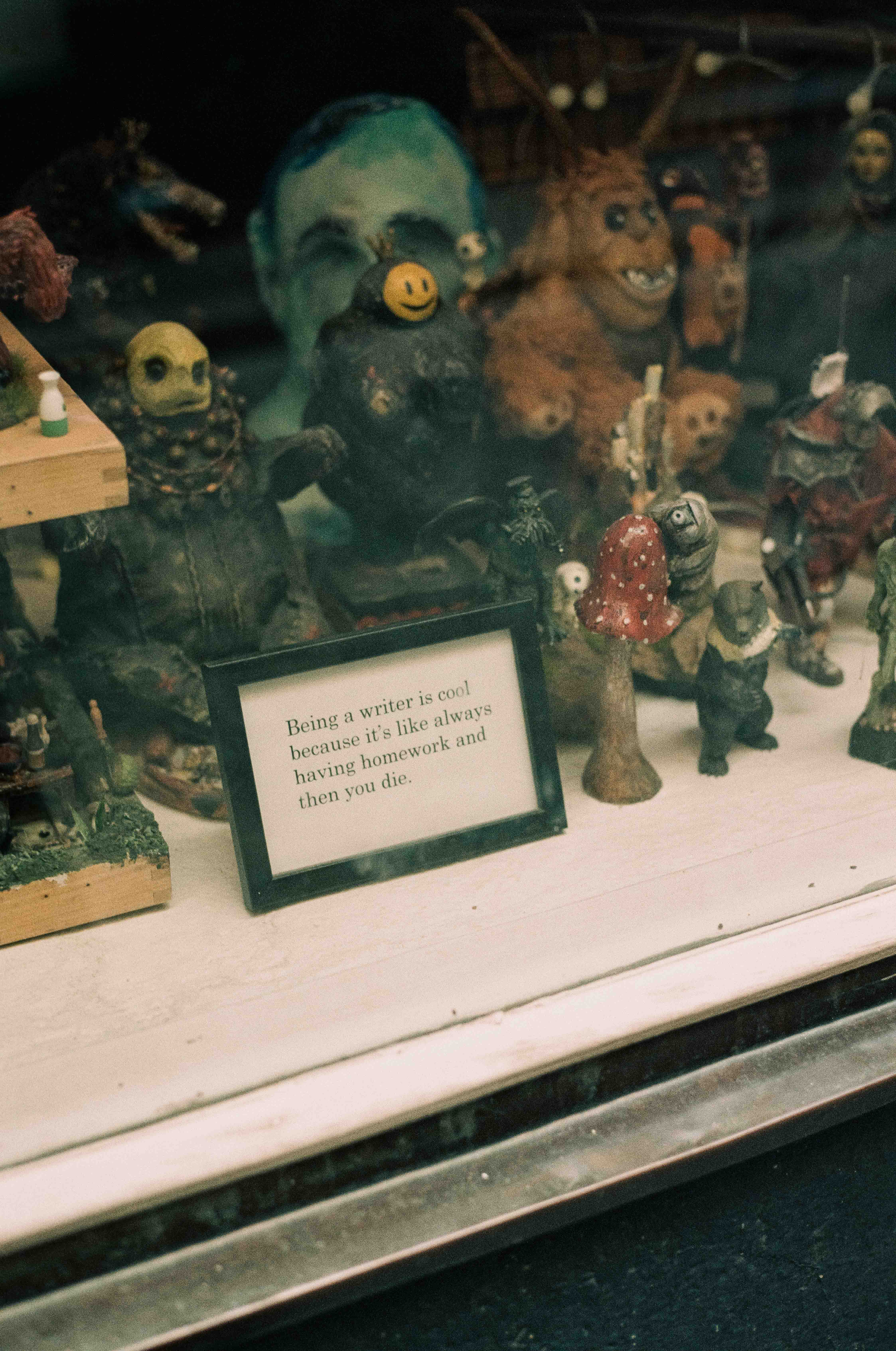 Figuras y muñecos en una vidriera, junto a un cartel enmarcado que compara escribir con tener deberes siempre.