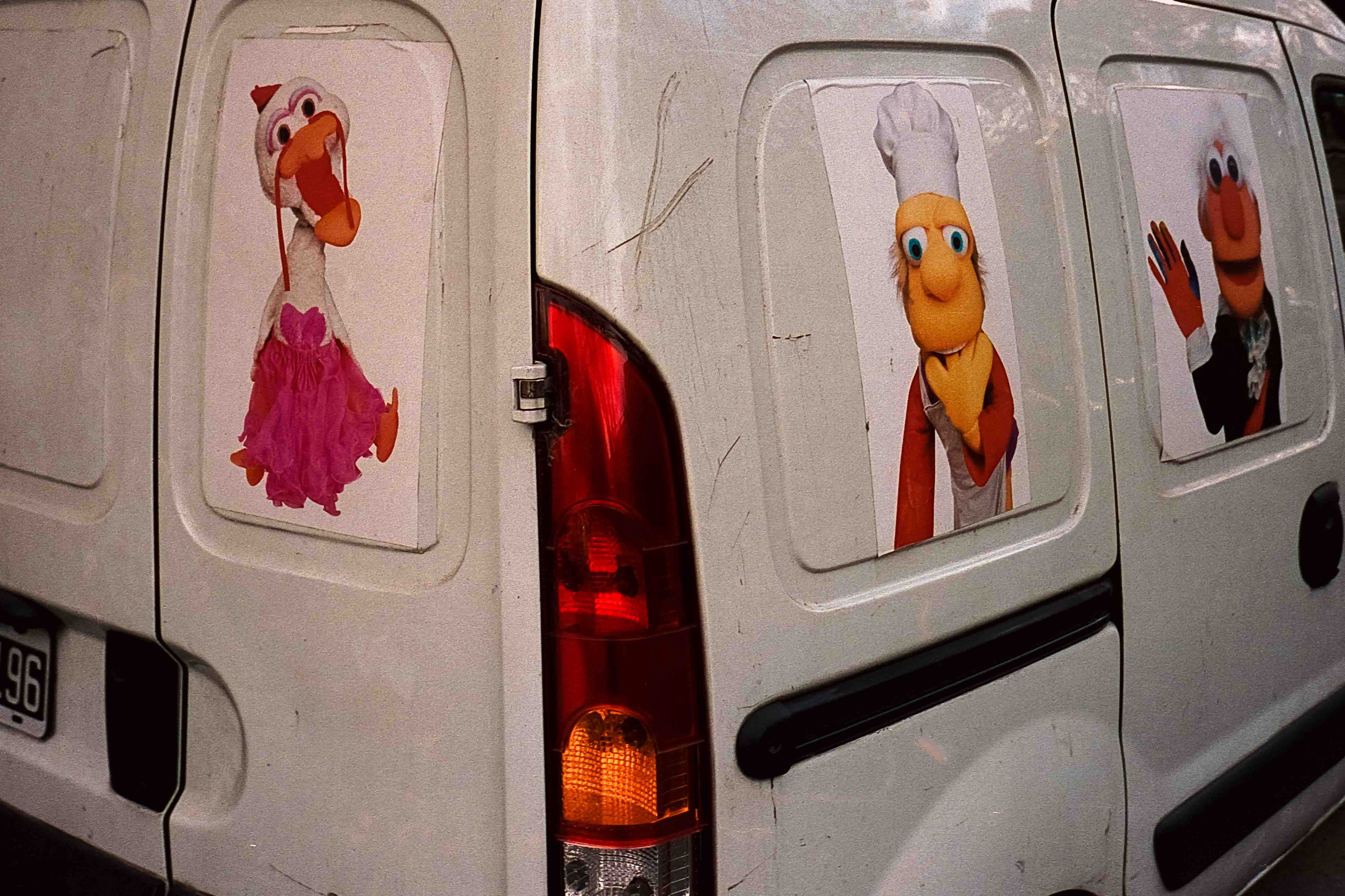 Furgoneta blanca con imágenes de personajes de títeres en sus ventanas traseras y laterales.