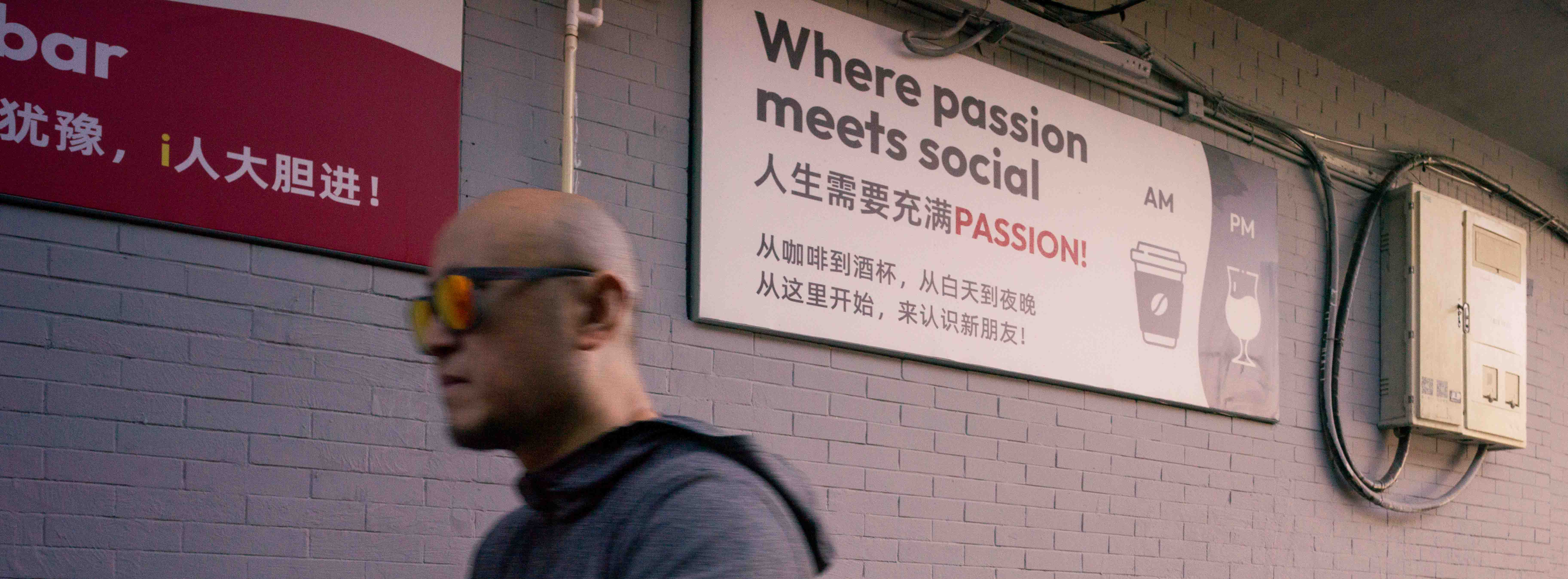 Persona con anteojos amarillos pasa frente a un cartel que dice «Where passion meets social».
