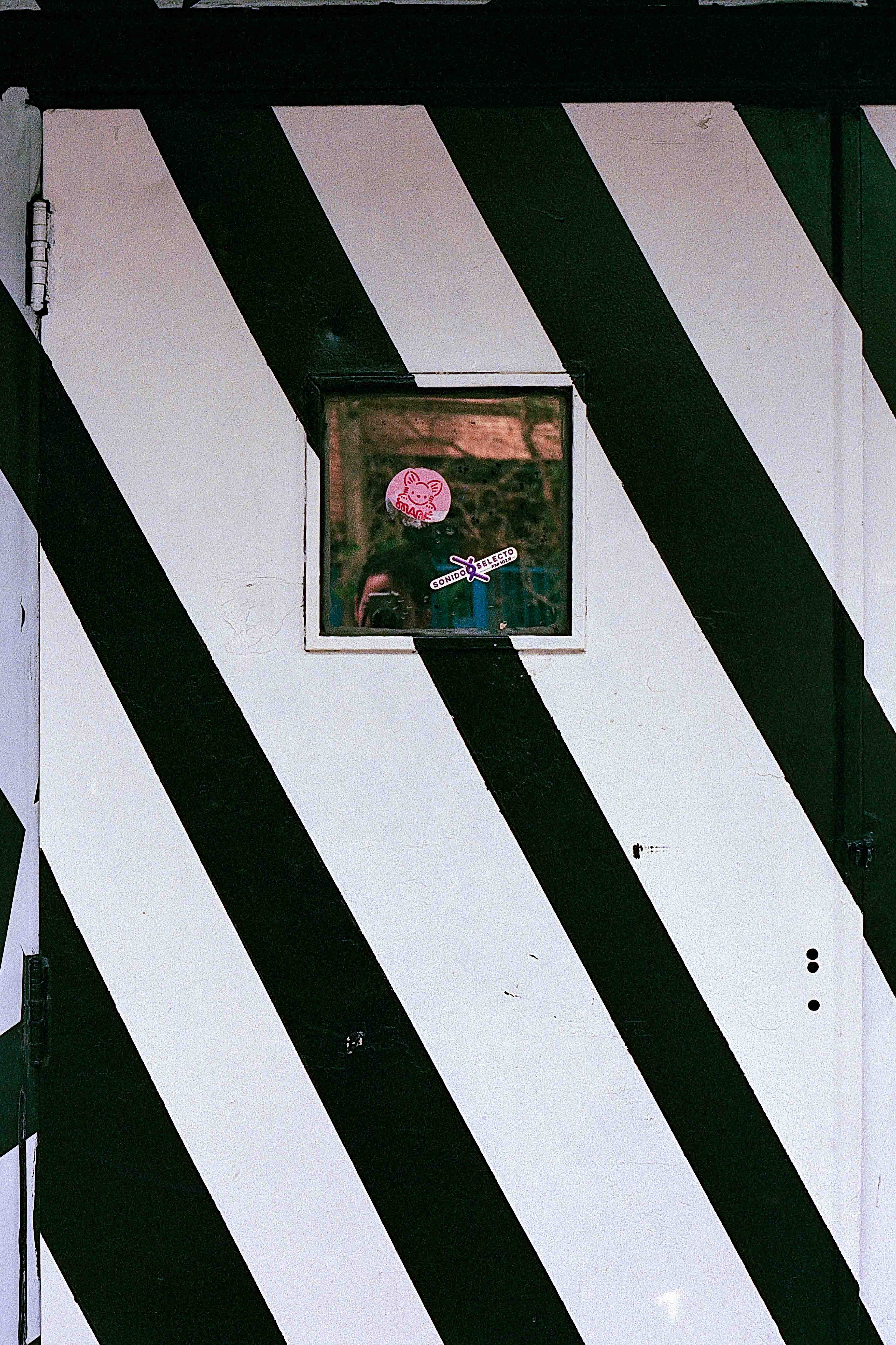 Pequeño espejo con un reflejo parcial en una puerta de grandes franjas diagonales negras y blancas.