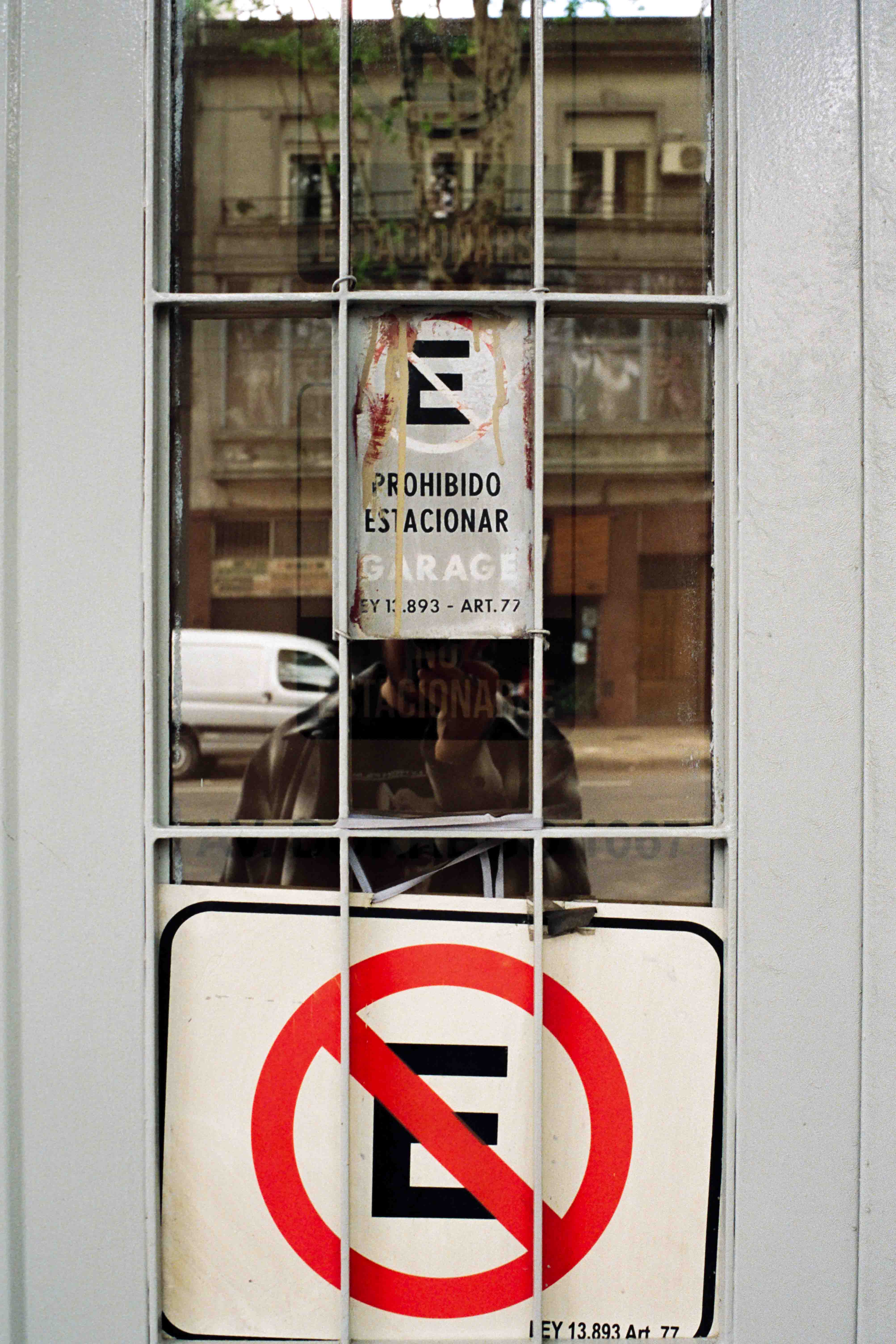 Autorretrato sobre puerta con cartel de prohibido estacionar