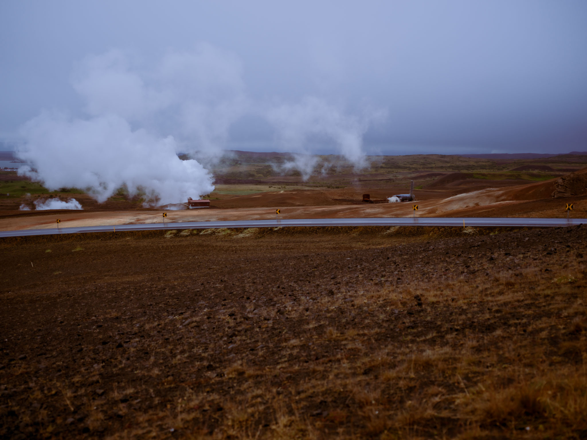 Grandes columnas de vapor se elevan sobre un terreno ocre junto a una carretera vacía.
