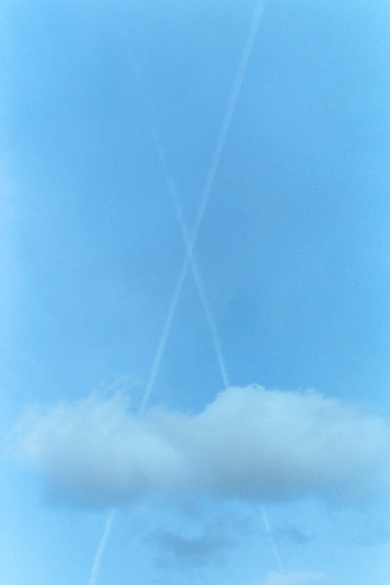 Dos estelas tenues de avión se cruzan en un cielo azul con nubes blancas en la parte inferior.
