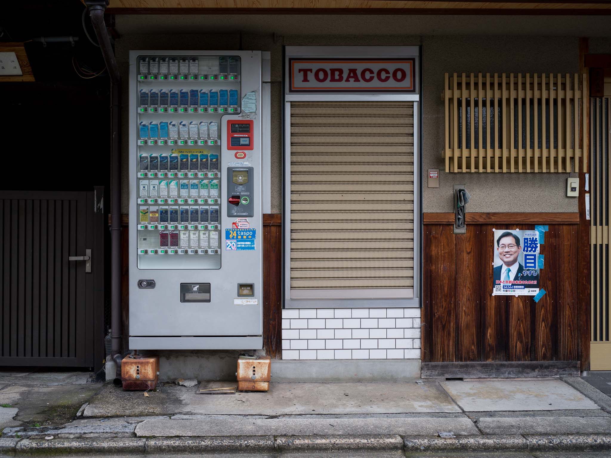 Máquina expendedora de cigarrillos junto a una persiana cerrada bajo un cartel que dice TOBACCO.