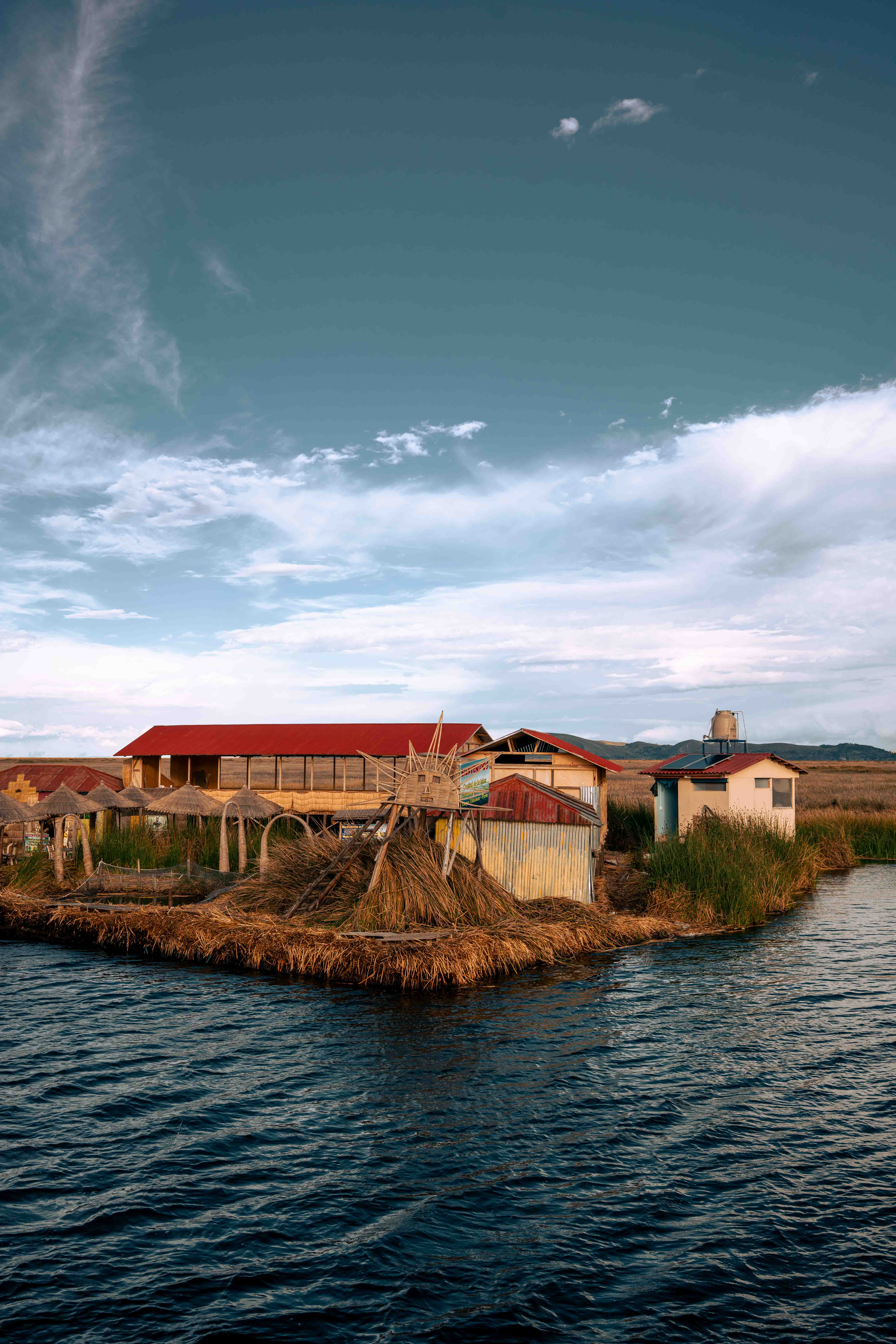 Pequeña isla de juncos con construcciones y un techo rojo, rodeada de agua bajo un cielo amplio.