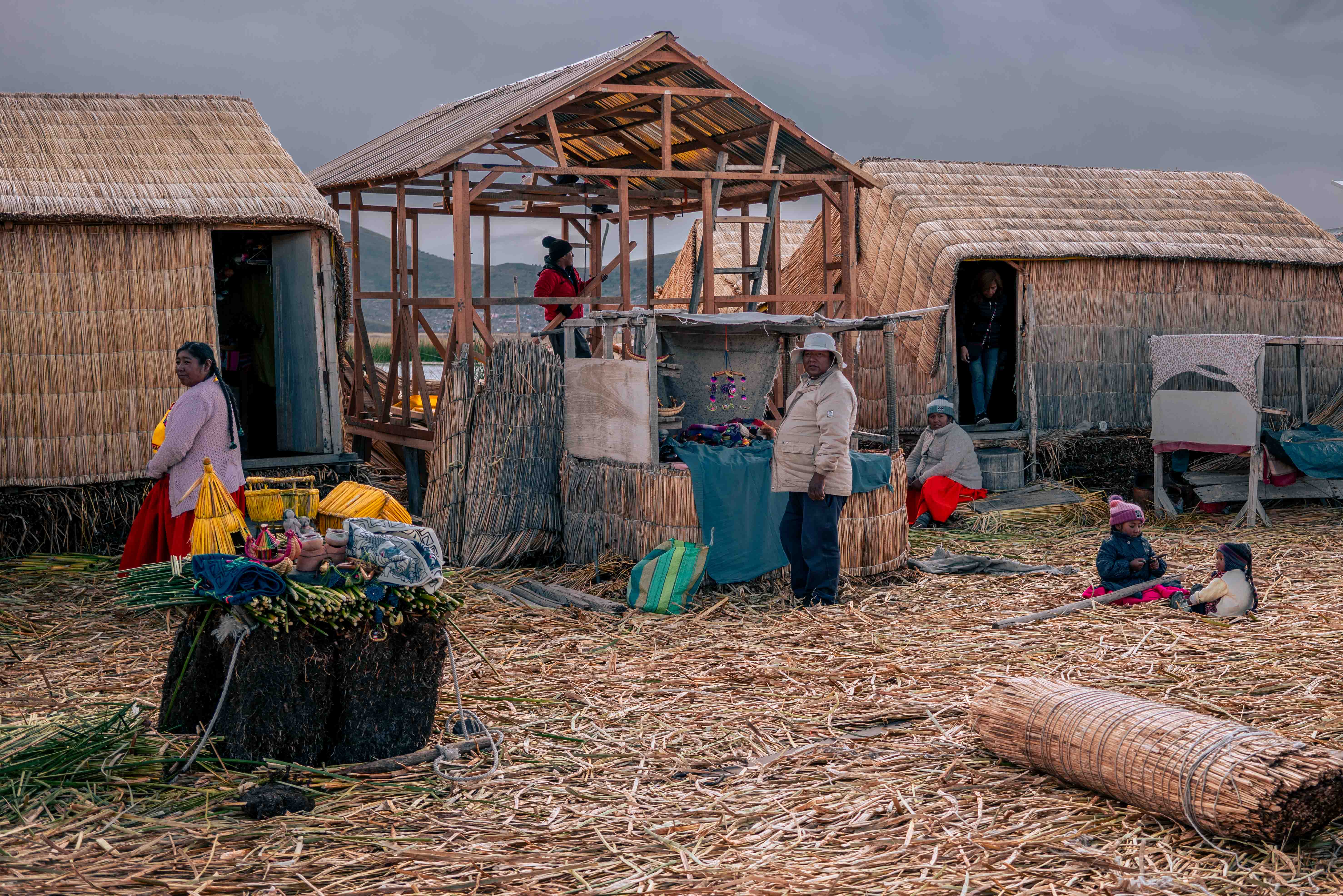 Varias personas entre casas de juncos y una estructura de madera en construcción.
