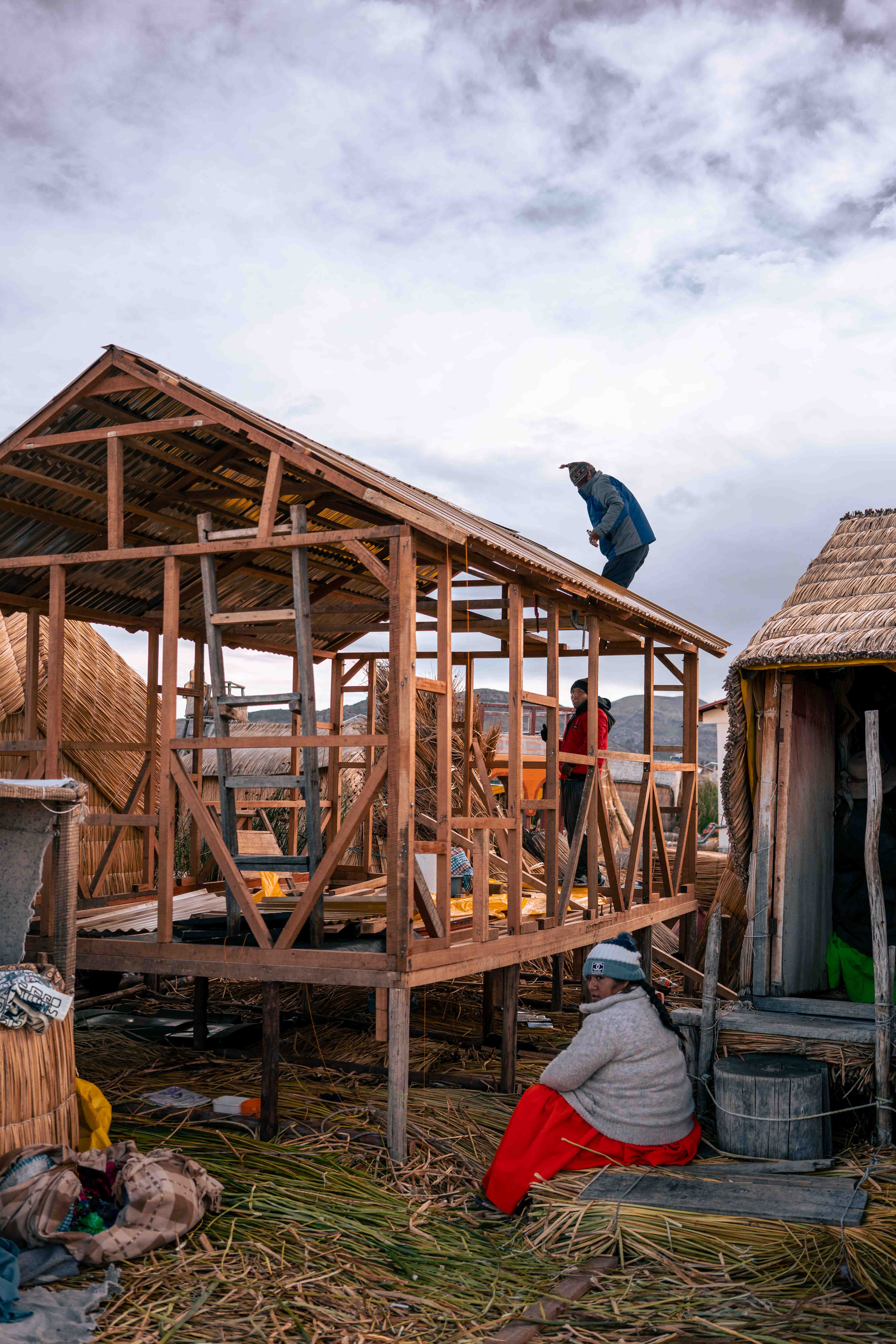 Personas alrededor de la estructura de madera de una casa, con un pájaro posado en el techo.