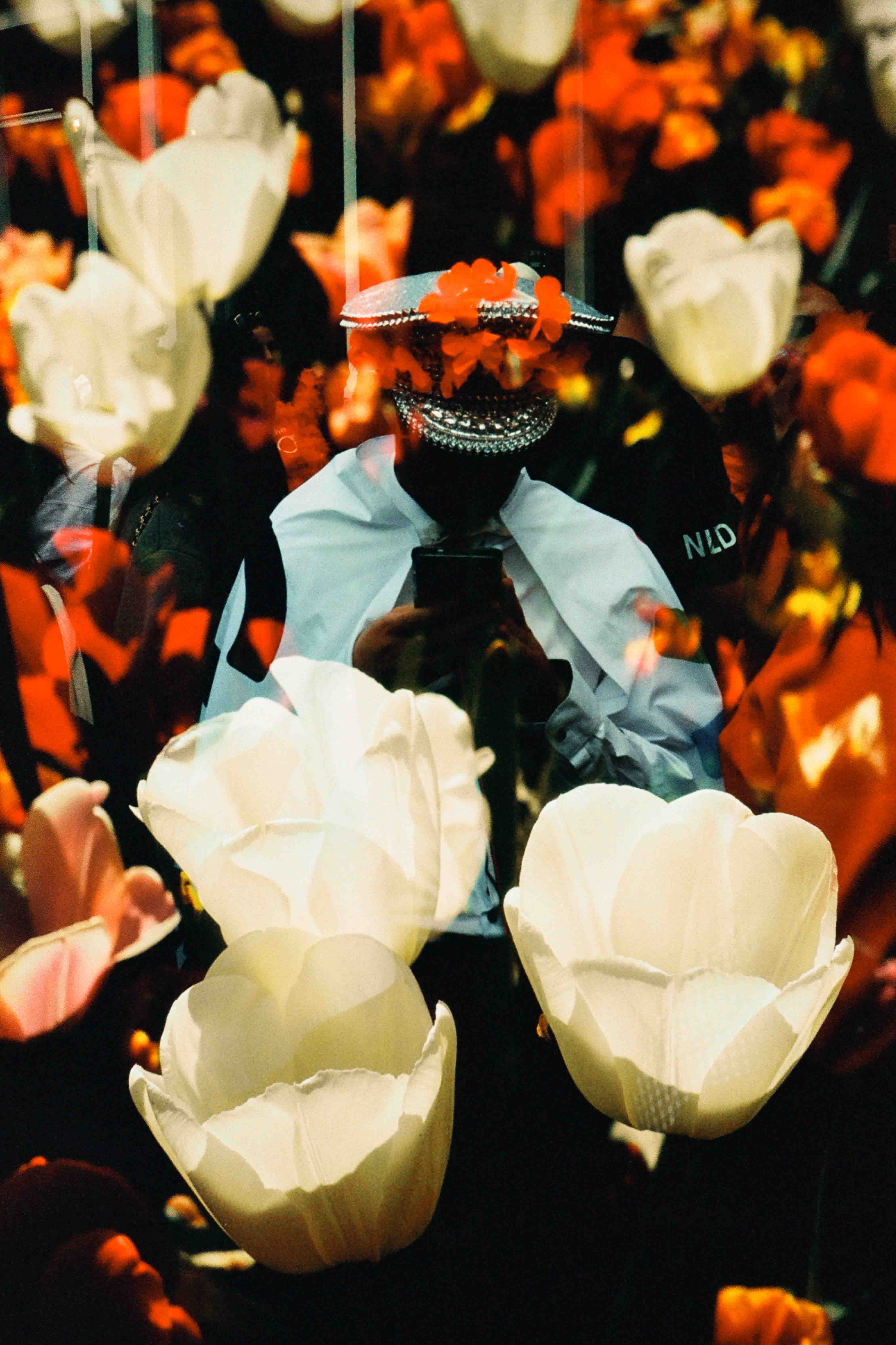 Persona con gorra blanca de capitán, camisa blanca y corbata negra mirando un teléfono, con flores blancas superpuestas.