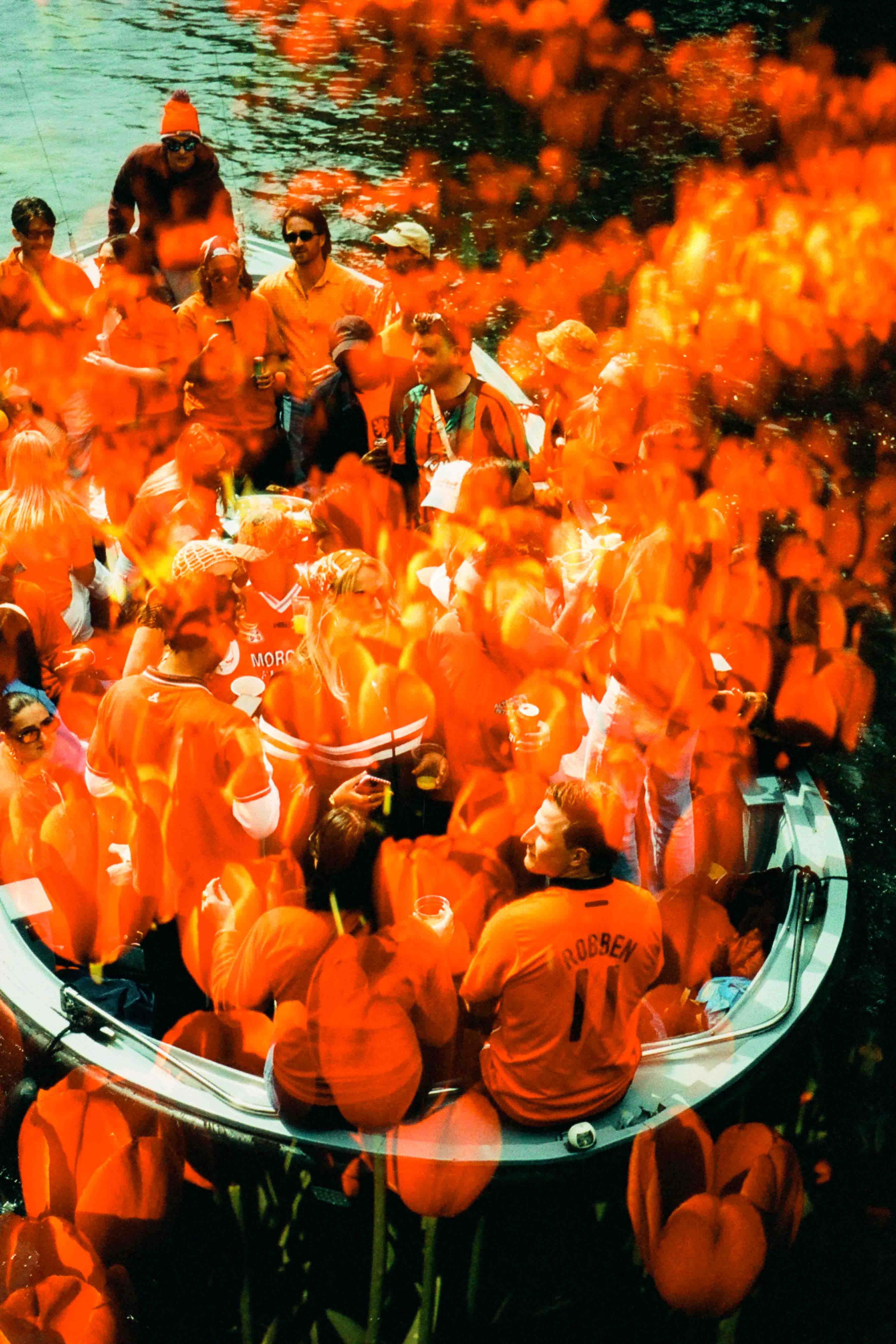 Grupo de personas vestidas de naranja en una embarcación, con flores naranjas superpuestas sobre la escena.